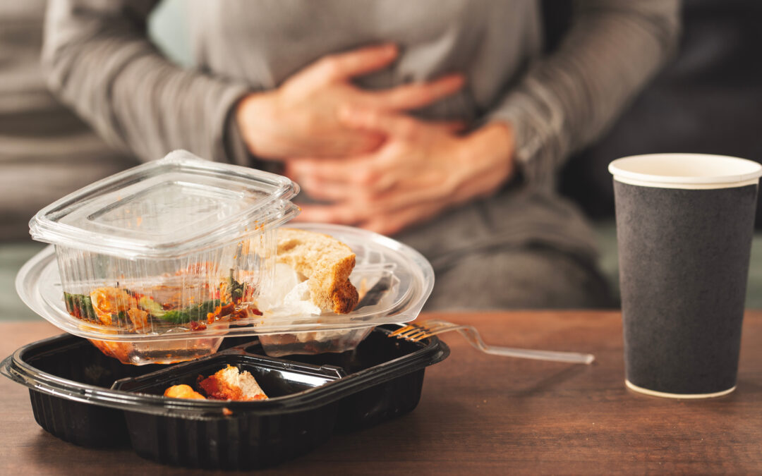 leftover takeout food containers on a table with a person clutching their stomach, representing food poisoning or a stomach virus.