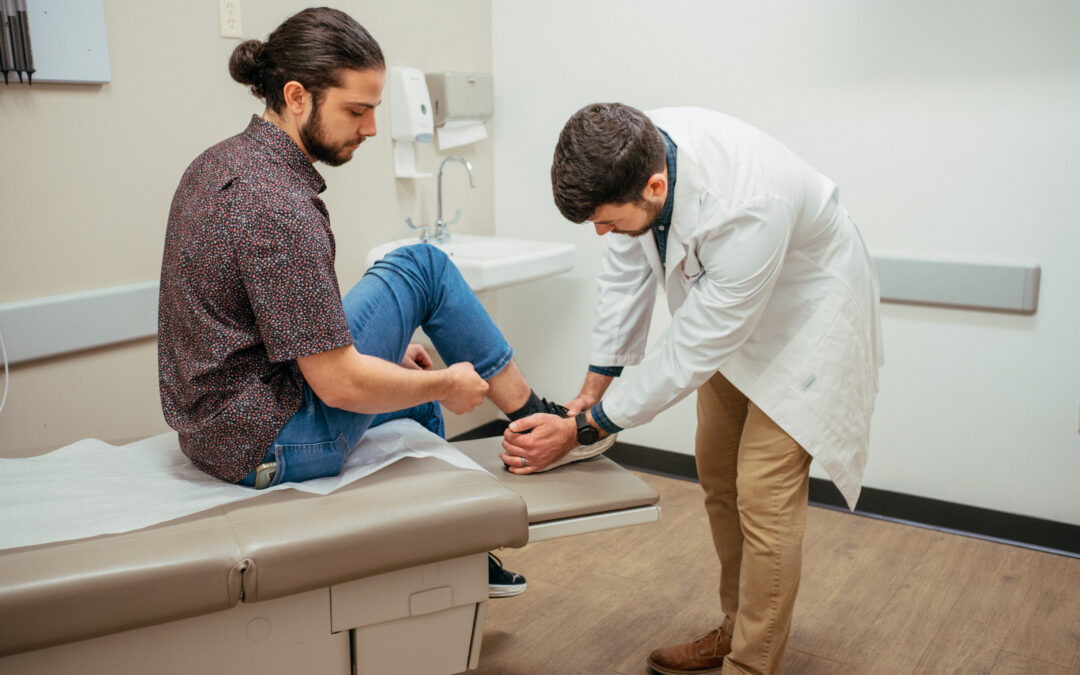 Male AFC healthcare provider examining a male patient’s right ankle and foot after a gardening accident in an examination room.
